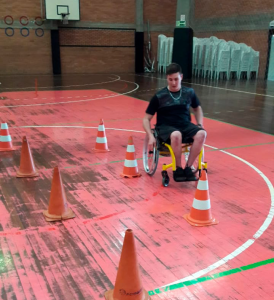Participante do Programa de Habilidades em Cadeira de Rodas em uma cadeira de rodas amarela dando a volta em cones laranjas.